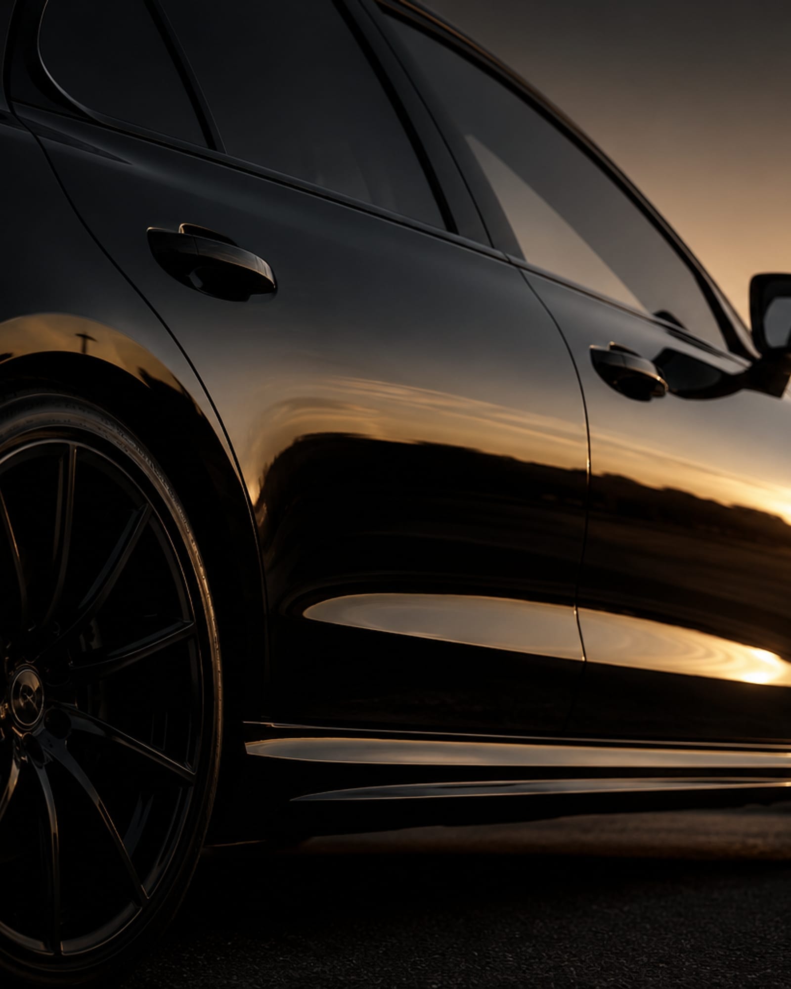 Side body line of a black luxury sedan at golden hour